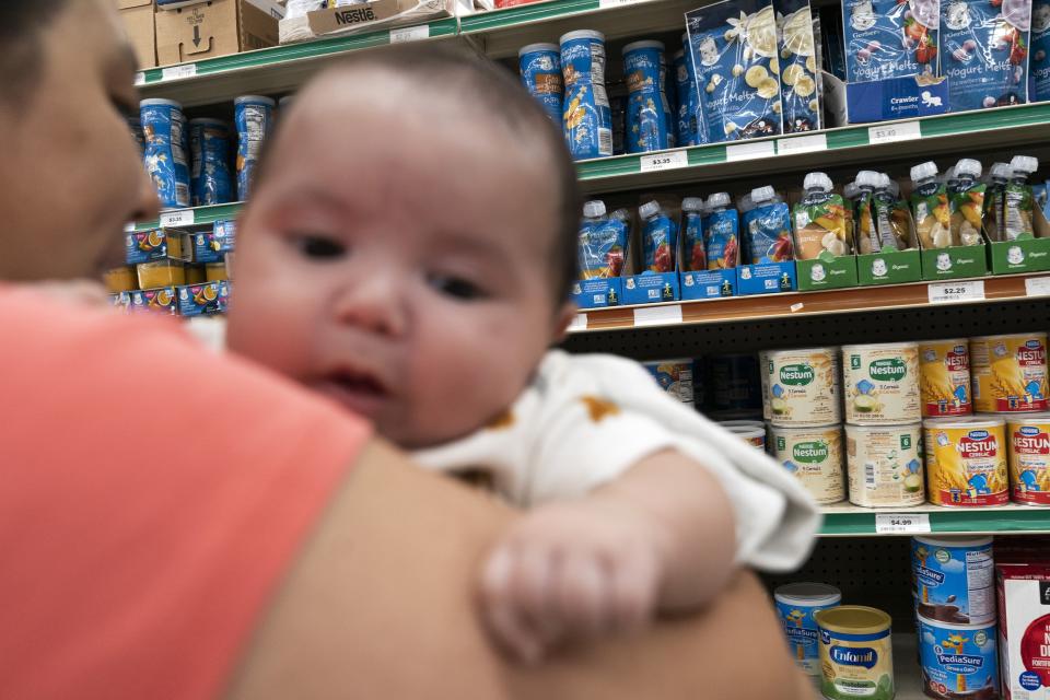 Yury Navas, 29, of Laurel, Md., looks for formula, while holding her two-month-old baby Ismael Galvaz, at Superbest International Market in Laurel, Md., Monday, May 23, 2022. After this day's feedings she will be down to their last 12.5 ounce container of formula. The only formula he can take without digestive issues, Enfamil Infant, has been close to impossible for her to find. Navas doesn't know why her breastmilk didn't come in for her third baby and has tried many brands of formula before finding the one kind that he could tolerate without digestive upset. Though the baby food aisle had plenty of options for older babies, the kind she needs was nowhere in sight. (AP Photo/Jacquelyn Martin)