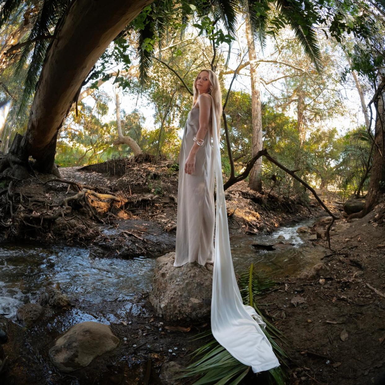 A woman in a long white dress stands in a park.