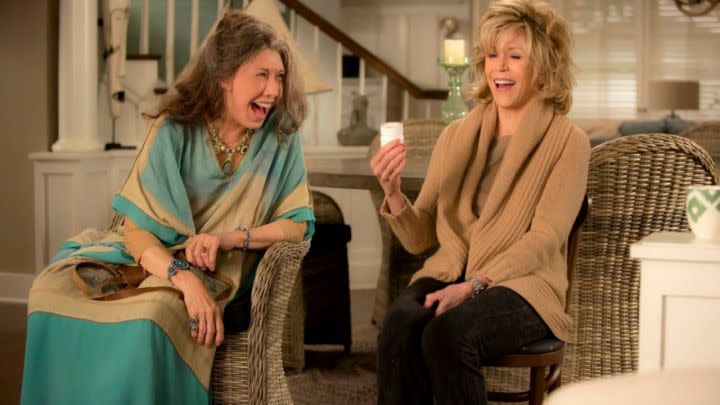 Lily Tomlin and Jane Fonda as Frankie and Grace laughing in their couch in Grace and Frankie.