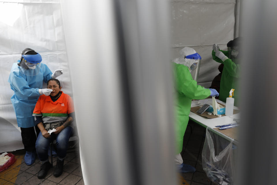 Dr. Victor Hugo Santamaria tests a woman for COVID-19 as nurses prepare to conduct tests, inside tents set up to perform rapid coronavirus testing at the TAPO bus station in the Venustiano Carranza borough of Mexico City, Friday, Nov. 20, 2020. Mexico passed the 100,000 mark in confirmed COVID-19 deaths on Thursday, becoming only the fourth country to do so. (AP Photo/Rebecca Blackwell)