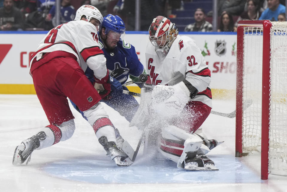 Carolina Hurricanes goalie Antti Raanta (32) makes a save as Brady Skjei, left, checks Vancouver Canucks' J.T. Miller during the second period of an NHL hockey game Saturday, Dec. 9, 2023, in Vancouver, British Columbia. (Darryl Dyck/The Canadian Press via AP)