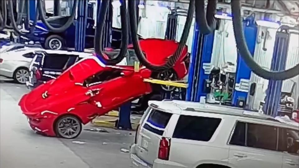 A red Chevrolet Corvette Z06 teetering off a garage lift after it has fallen.