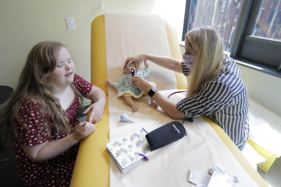 Emilyanne Wade, 12, left, looks on as Tricia Nora, a pediatric nurse practitioner, examines Sophia, Wade's baby doll, Wednesday, June 17, 2020, in a medical clinic at Mary's Place, a family homeless shelter located inside an Amazon corporate building on the tech giant's Seattle campus. The facility is home to the Popsicle Place shelter program, an initiative to address the needs of homeless children with life-threatening health conditions. (AP Photo/Ted S. Warren)