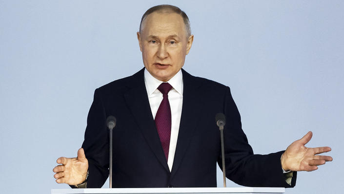 ولادیمیر پوتین، رئیس‌جمهور روسیه در حالی که پشت سکو ایستاده است، اشاره می‌کند.