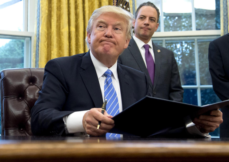 President Donald Trump signs an executive order as Chief of Staff Reince Priebus looks on in the Oval Office of the White House in Washington, DC, January 23, 2017. Trump on Monday signed three orders on withdrawing the US from the Trans-Pacific Partnership trade deal, freezing the hiring of federal workers and hitting foreign NGOs that help with abortion.&nbsp;