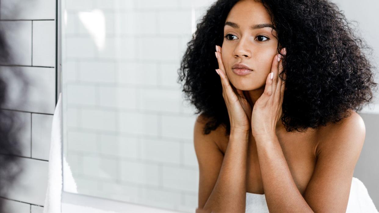 mixed race woman massaging her face and looking at a mirror