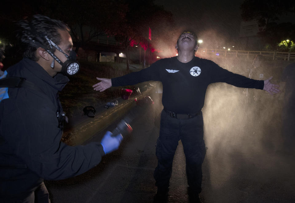 El paramédico Óscar Becerril descontamina a su compañero César Ávila después de una llamada nocturna para recoger a un paciente con COVID-19, en su base Troya en Iztapalapa, un distrito de la Ciudad de México, el sábado 30 de mayo de 2020. (Foto AP/Marco Ugarte)