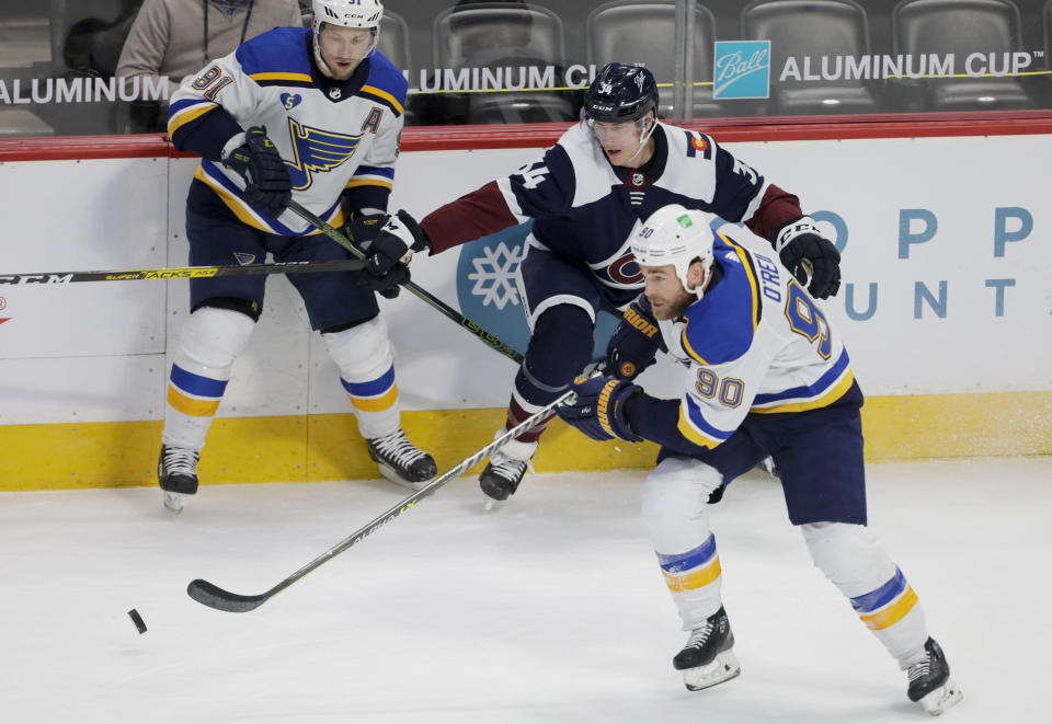 St. Louis Blues center Ryan O'Reilly (90) skates the puck away from Colorado Avalanche defenseman Jacob MacDonald (34) and Blues right wing Vladimir Tarasenko (91) during the second period of an NHL hockey game in Denver, Saturday, April 3, 2021. (AP Photo/Joe Mahoney)