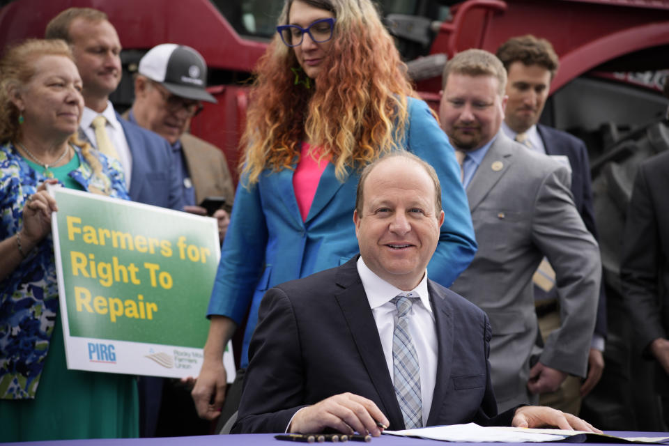 Colorado Gov. Jared Polis, front, waits to sign legislation that forces manufacturers to provide the necessary manuals, tools, parts and even software to farmers so they can fix their own machines, Tuesday, April 25, 2023, during a ceremony outside the State Capitol in Denver. Colorado is the first state to put the right-to-repair law into effect while at least 10 other states are considering similar measures. Colorado State Rep. Brianne Titone, center, and Rep. Ron Weinberg, back, head in to witness the signing. (AP Photo/David Zalubowski)