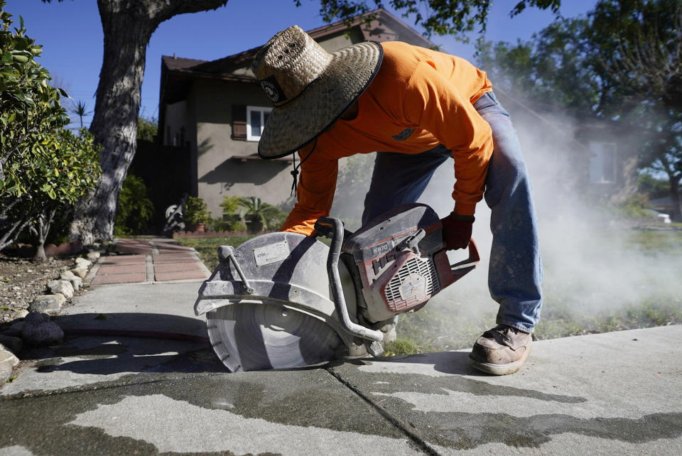Contractor Jesse De Loera cuts a concrete sidewalk in Upland, Calif., on Monday, Jan. 24, 2022. After estimating a loss in revenue in the early months of the pandemic in 2020, city officials say Upland is now doing well financially, boosted partly by federal pandemic aid. The city plans to use part of that aid to repave parking lots and repair hundreds of sections of sidewalks. (AP Photo/Damian Dovarganes)