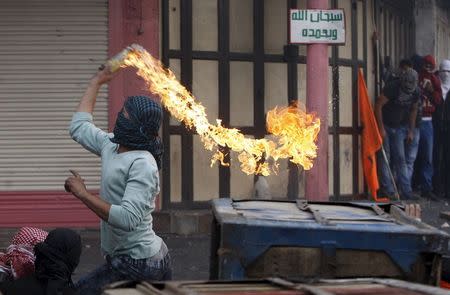 A masked Palestinian protester throws a molotov cocktail at Israeli troops during clashes in the West Bank city of Hebron October 10, 2015. REUTERS/Mussa Qawasma