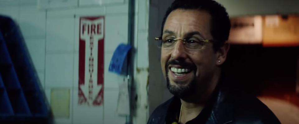 Adam Sandler as Howard in 'Uncut Gems' smiling in a building backroom