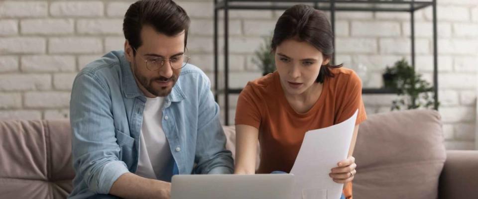 Focused young couple looking at computer screen, sitting on couch, planning finances.