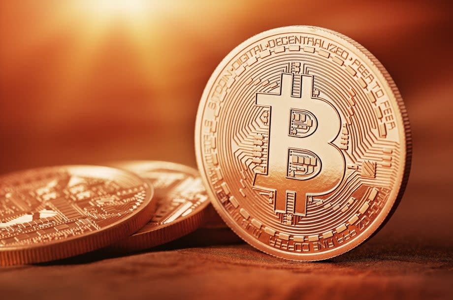 Physische Repräsentanz einer Bitcoin-Münze auf güldenem Hintergrund.