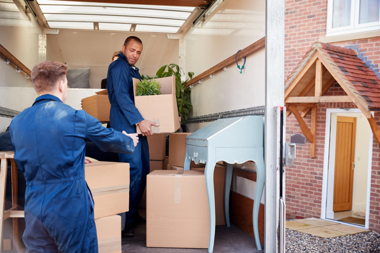 Removal Company Workers Unloading Furniture And Boxes From Truck Into New Home On Moving Day