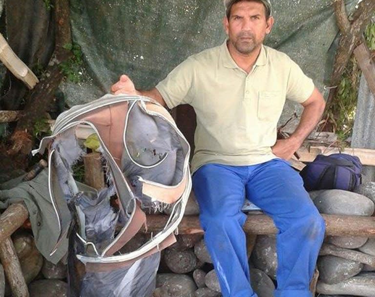 Johnny Begue, a member of a local shore cleaning association, displays the remains of a suitcase found along with a piece of plane wreckage on July 30, 2015 in Saint-Andre, La Reunion