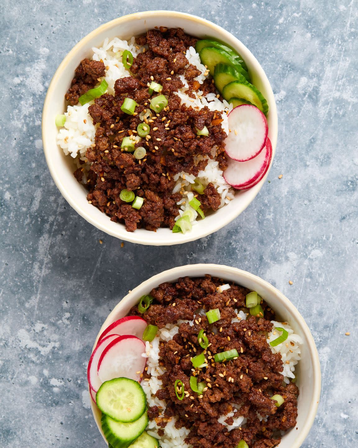 two bowls of caramelized beef over white rice garnished with radishes and cucumbers