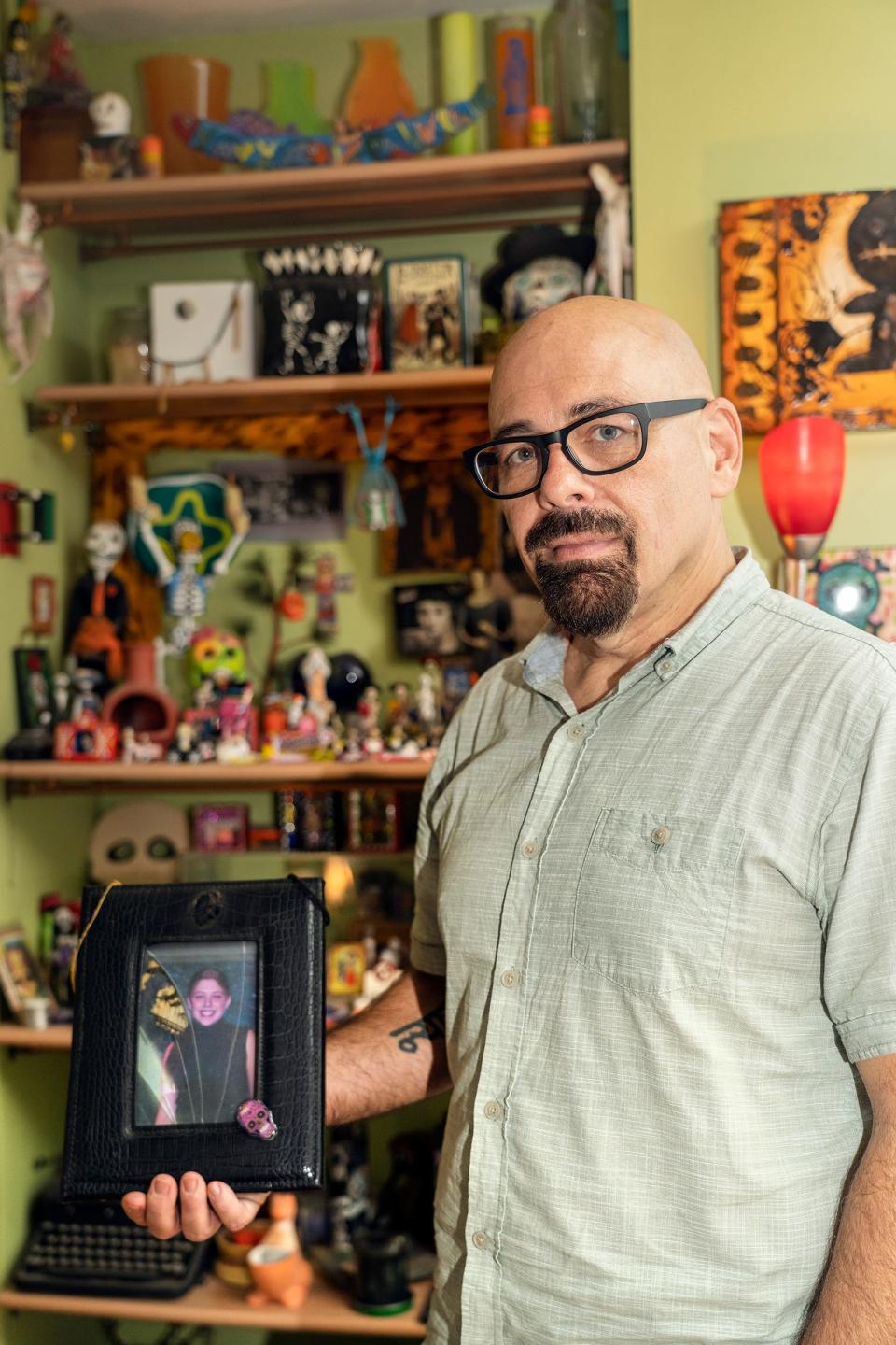 Drew Crecente holds a picture frame with a photo of his daughter, Jennifer Crecente, in front of the D’a de los Muertos ofrenda at his home in Atlanta, Georgia Monday, July 31, 2023. Drew touches the top of the frame to say goodbye to Jennifer every day before leaving the house. He also travels with the photo whenever he takes trips.