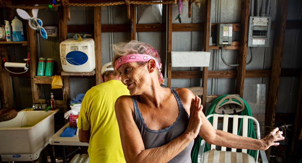 Michele Bryant cools off using a small fan at the shrimp docks on Fort Myers Beach on July 26. She works on the docks helping wherever needed. She has been living in a tent in front of the shrimp docks since Hurricane Ian slammed ashore in September of last year. This recent heat wave put her in the hospital twice with heat related symptoms, she says.