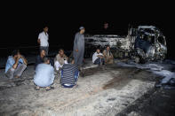 People stand near burned vehicles following a fire that broke out in the Shuqair-Mostorod crude oil pipeline, on the Cairo-Ismailia road, in Egypt, Tuesday, July 14, 2020. A ruptured crude oil pipeline set off a monstrous blaze on a desert highway in Egypt on Tuesday, injuring at least 17 people, local authorities said. (AP Photo/Alaa Ahmed)