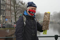 A man with an Amsterdam face mask holds a free bouquet of tulips in Amsterdam, Netherlands, Saturday, Jan. 15, 2022. Stores across the Netherlands cautiously re-opened after weeks of coronavirus lockdown, and the Dutch capital's mood was further lightened by dashes of color in the form of thousands of free bunches of tulips handed out by growers sailing with a boat through the canals. (AP Photo/Peter Dejong)