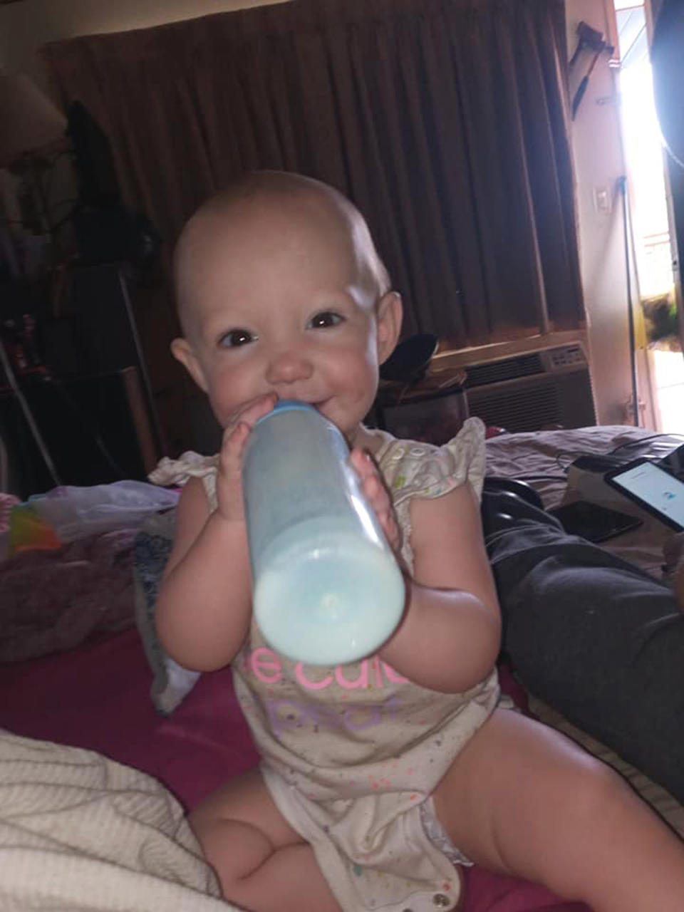 A baby girl (Mercedes) smiling looking at camera with a bottle in her mouth.