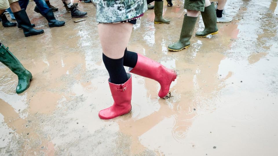 A picture shows someone wearing bright red wellies walking through a muddy puddle at the festival. 