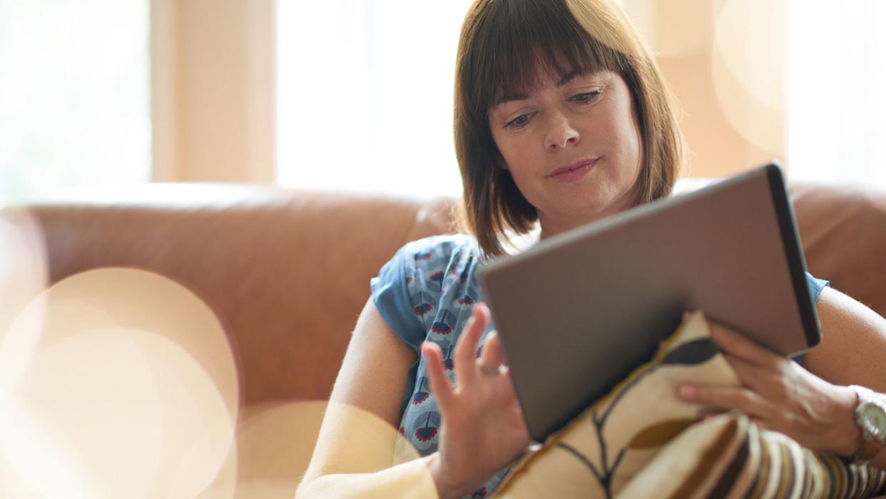 Serene lady in her forties reading emails on a wireless tablet in a brightly lit house- filtered image.