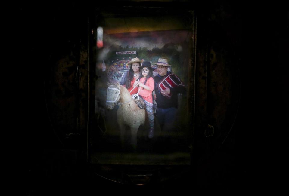 En esta imagen del 4 de septiembre de 2016, una familia vista a través de la vieja cámara de cajón de Luis Maldonado, en una feria que celebra el Día de Independencia de Chile en Santiago de Chile. A unos 7,50 dólares por retrato, una fotografía de cajón cuesta más del doble de los tres dólares que cuesta una digital. (AP Foto/Esteban Félix)