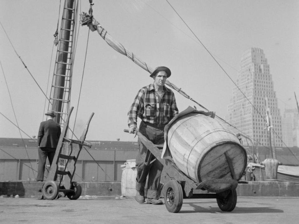 Dock stevedore at the Fulton fish market moving a barrel of codfish.