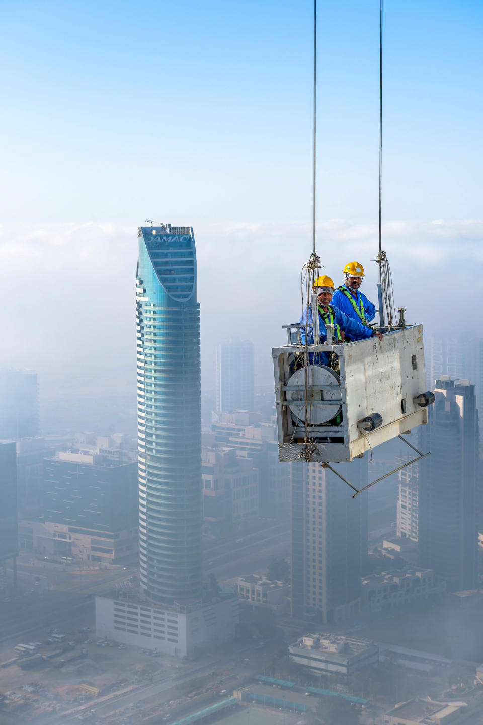 The workmen show no signs of fear as they dangle in a crib suspended by two cords 900ft above the street below. (SWNS)