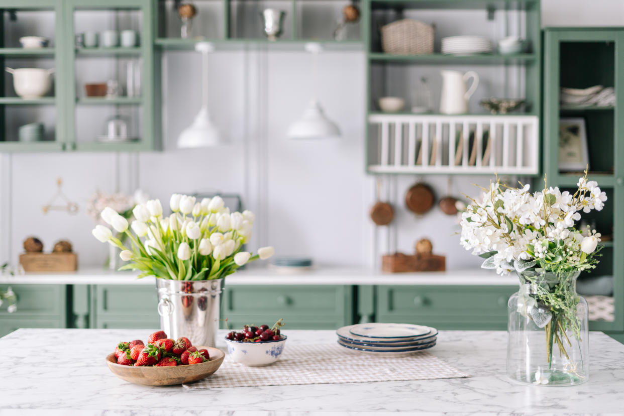  A kitchen with two vases of flower on a marble island. 