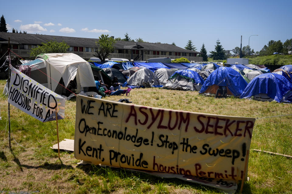 Signs adorn the front of an encampment of asylum-seekers mostly from Venezuela, Congo and Angola next to an unused motel owned by the county, Wednesday, June 5, 2024, in Kent, Washington. The group of about 240 asylum-seekers is asking to use the motel as temporary housing while they look for jobs and longer-term accommodations. (AP Photo/Lindsey Wasson)
