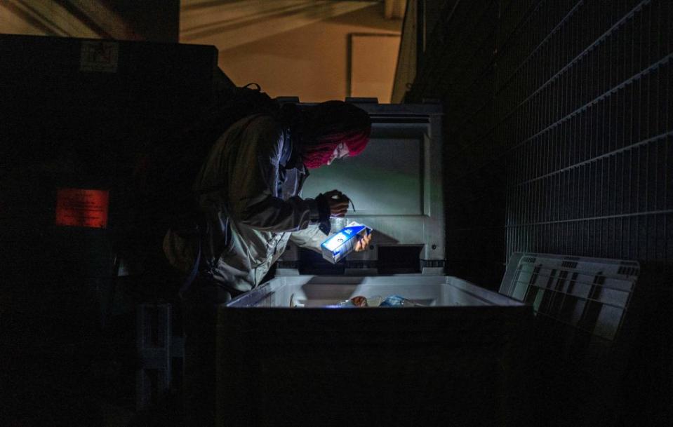 A dumpster diver picks through discarded food in the dark.