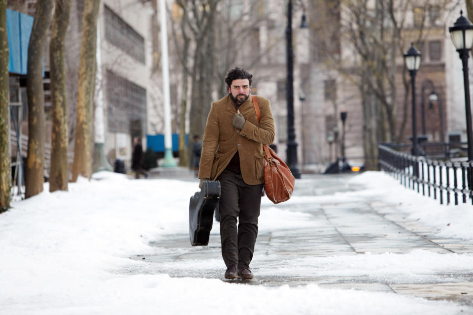 oscar isaac as llewyn davis bundled up walking down a snowy street with his guitar