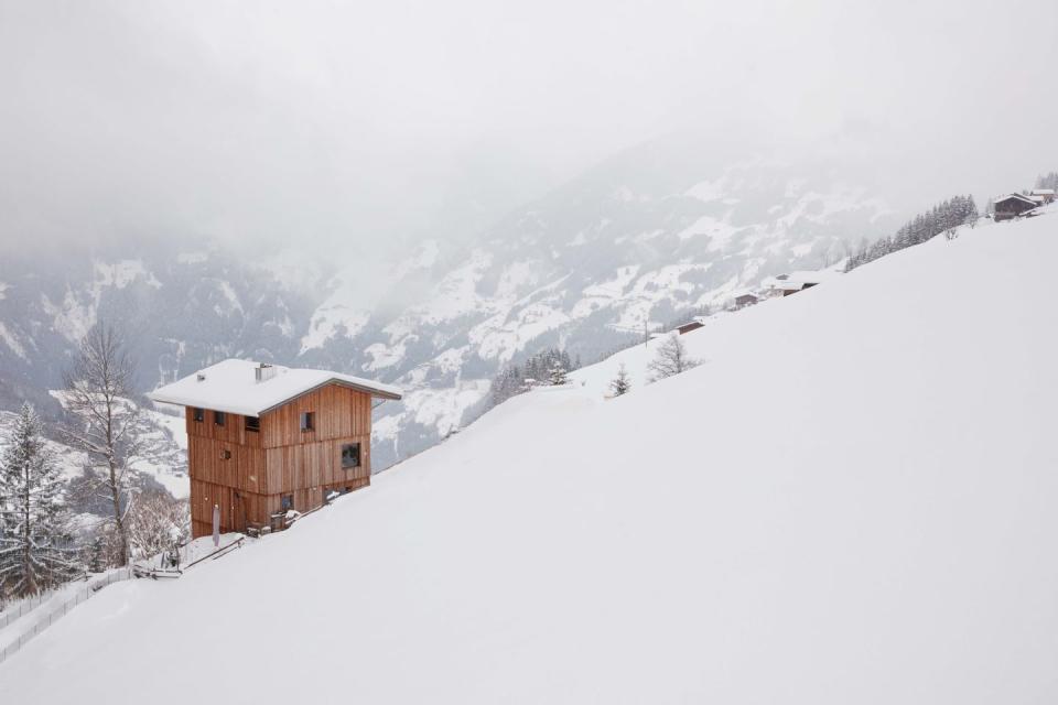 small isolated timber cabin on a snow covered hill surrounded by mountains