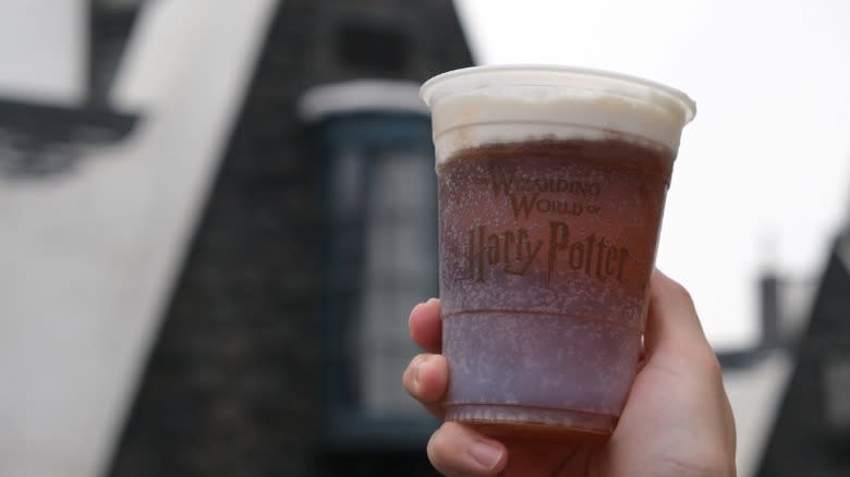 A hand holding up a cup of butterbeer 