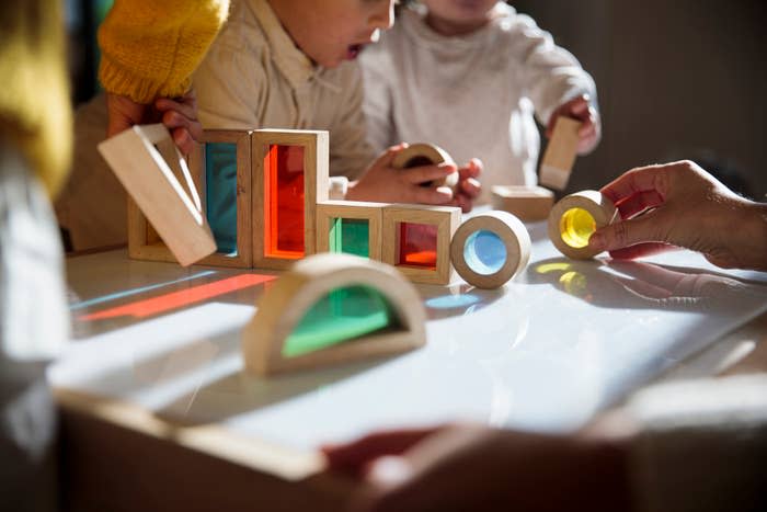 Children playing with wooden blocks and shapes on a table, with an adult's hand visible