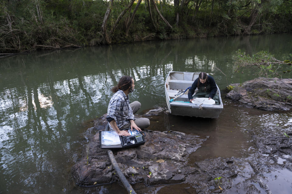 Two people searching for platypus in a river. One is in a boat.