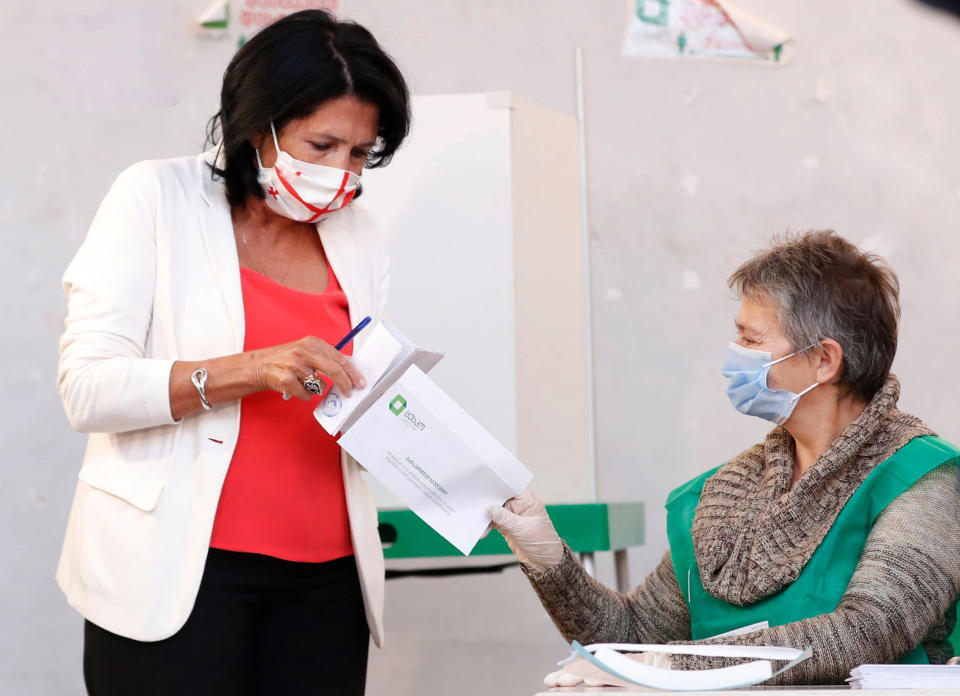 Georgia's President Salome Zurabishvili, left, wearing a face mask to help curb the spread of the coronavirus, holds her ballot preparing to vote at a polling station during the parliamentary elections in Tbilisi, Georgia, Saturday, Oct. 31, 2020. The hotly contested election between the Georgian Dream party, created by billionaire Bidzina Ivanishvili who made his fortune in Russia and has held a strong majority in parliament for eight years, and an alliance around the country's ex-president who is in self-imposed exile in Ukraine. (AP Photo/Shakh Aivazov)