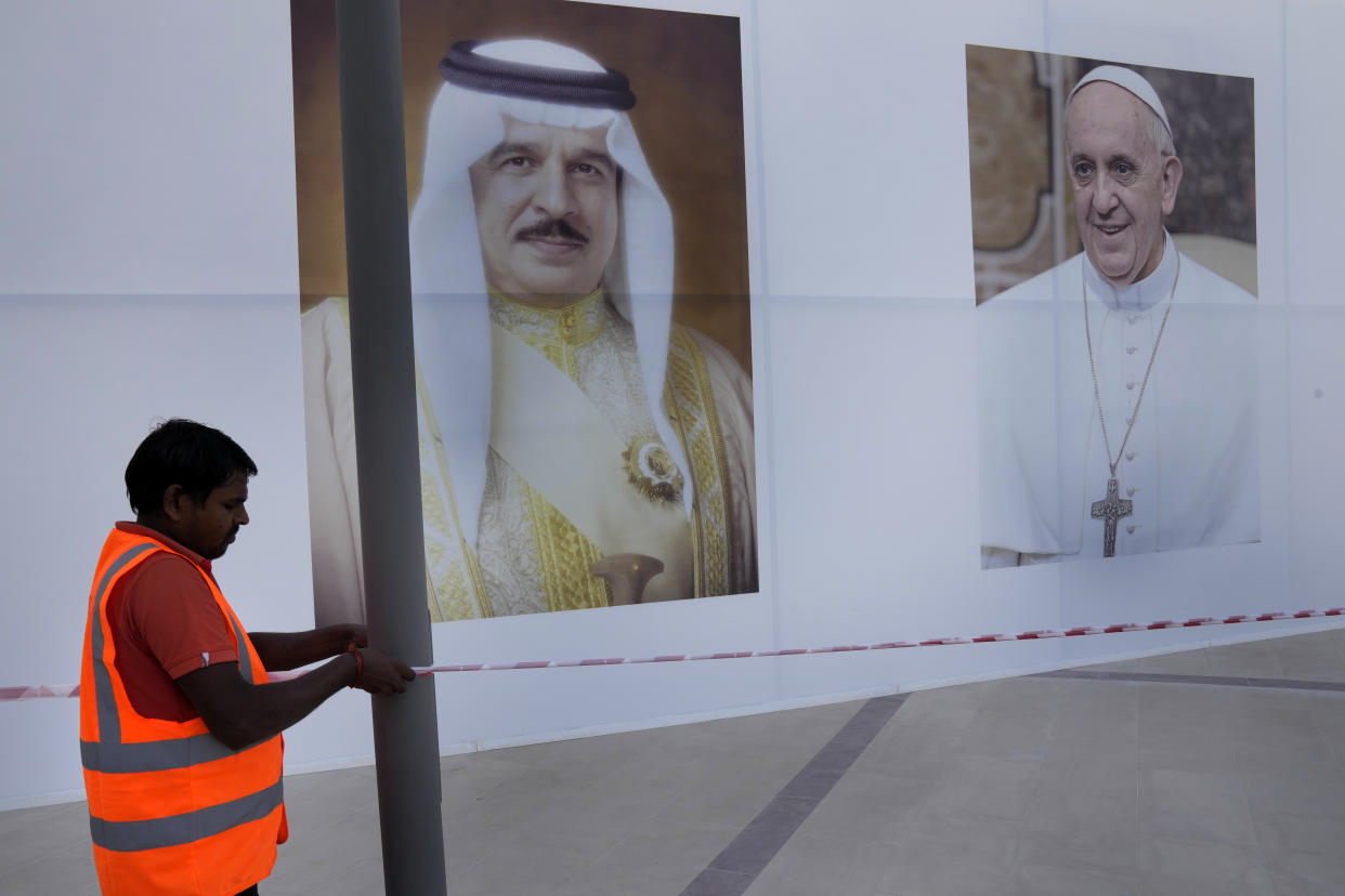 A worker hang a bar in front of portraits that show Pope Francis, right and Bahrain's King Hamad bin Isa Al Khalifa, left, outside the Cathedral of Our Lady of Arabia where the Pope will attend a Mass, in Manama, Bahrain, Wednesday, Nov. 2, 2022. Pope Francis is making the November 3-6 visit to participate in a government-sponsored conference on East-West dialogue and to minister to Bahrain's tiny Catholic community, part of his effort to pursue dialogue with the Muslim world. (AP Photo/Hussein Malla)