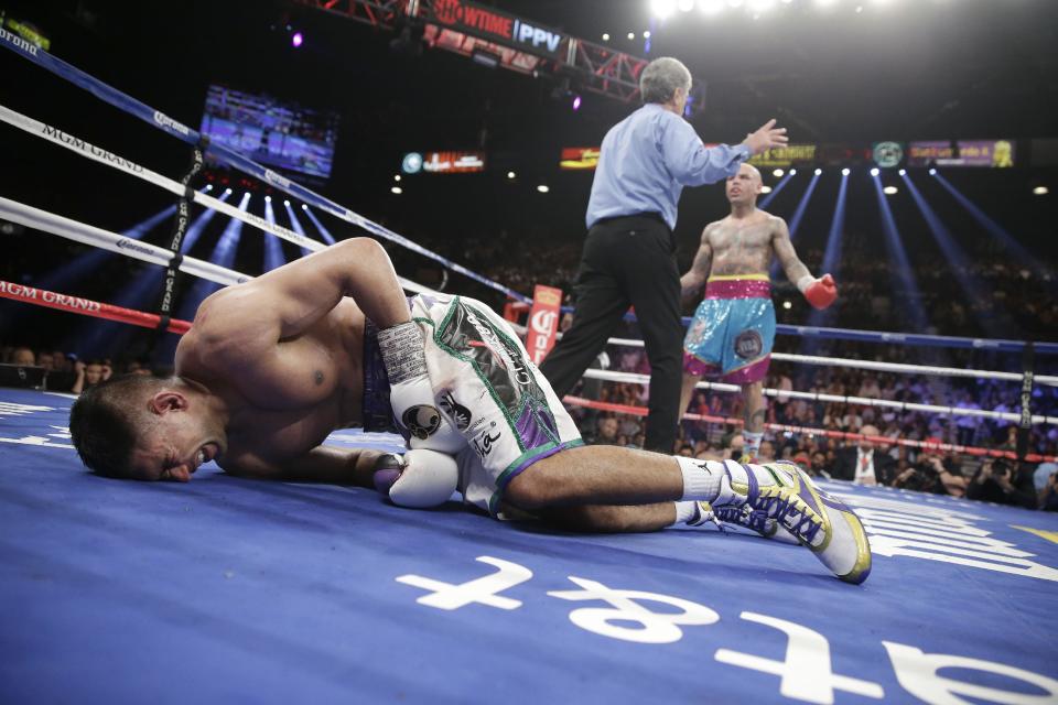 England's Amir Khan, left, crumbles to the mat after receiving a low blow from Luis Collazo, right, in their silver welterweight title boxing fight Saturday, May 3, 2014, in Las Vegas. Referee Vic Drakulich is at center. Khan went on to win by unanimous decision. (AP Photo/Isaac Brekken)