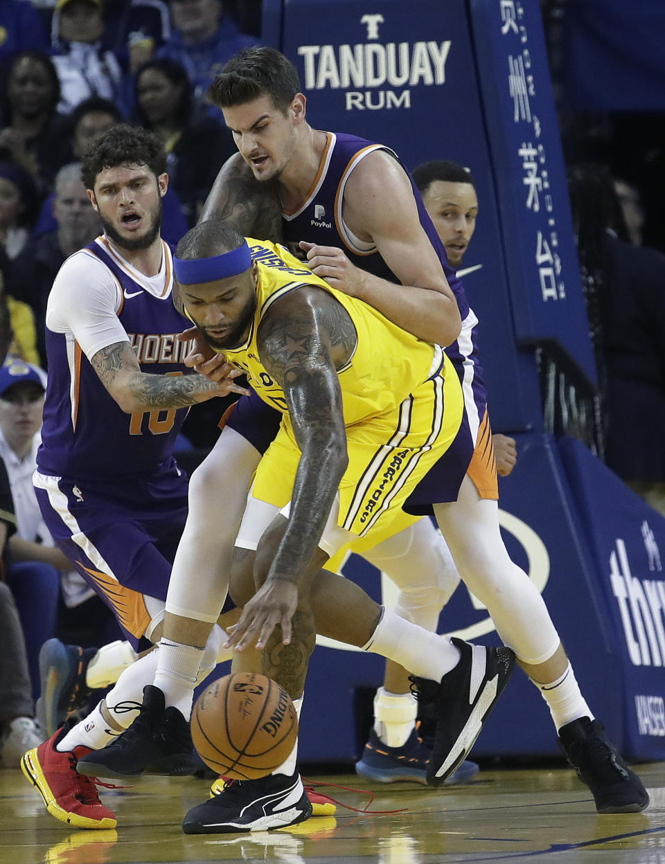 Golden State Warriors center DeMarcus Cousins, center, reaches for the ball in front of Phoenix Suns guard Tyler Johnson, left, and forward Dragan Bender during the first half of an NBA basketball game in Oakland, Calif., Sunday, March 10, 2019. (AP Photo/Jeff Chiu)