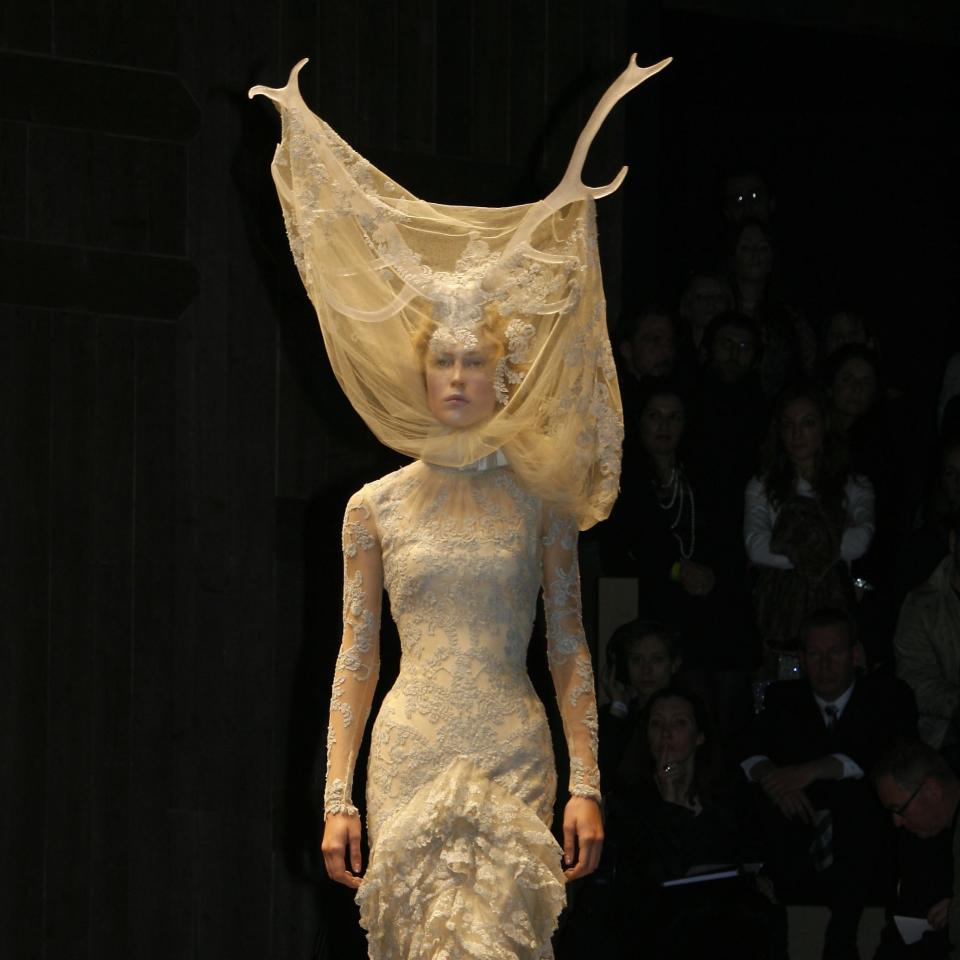 Model in elaborate textured gown with high ruffled collar and antler-like headpiece at a fashion show