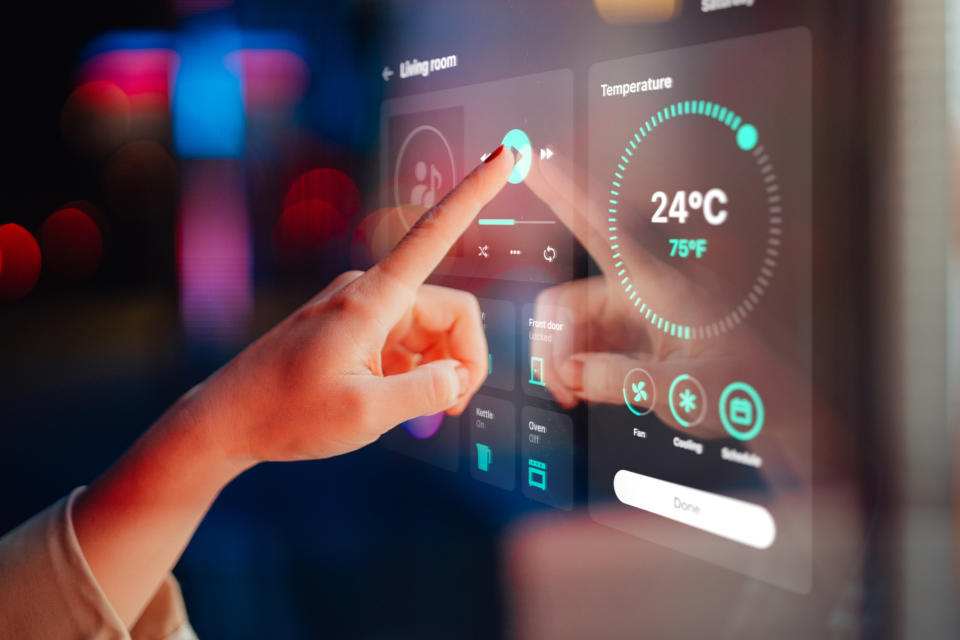 Close-up shot of a woman hand controlling smart home appliances with control panel in the living room of a modern home. Smart home technology concept. Smart living. Lifestyle and technology. Smart home dashboard - using a control panel of a modern smart home.