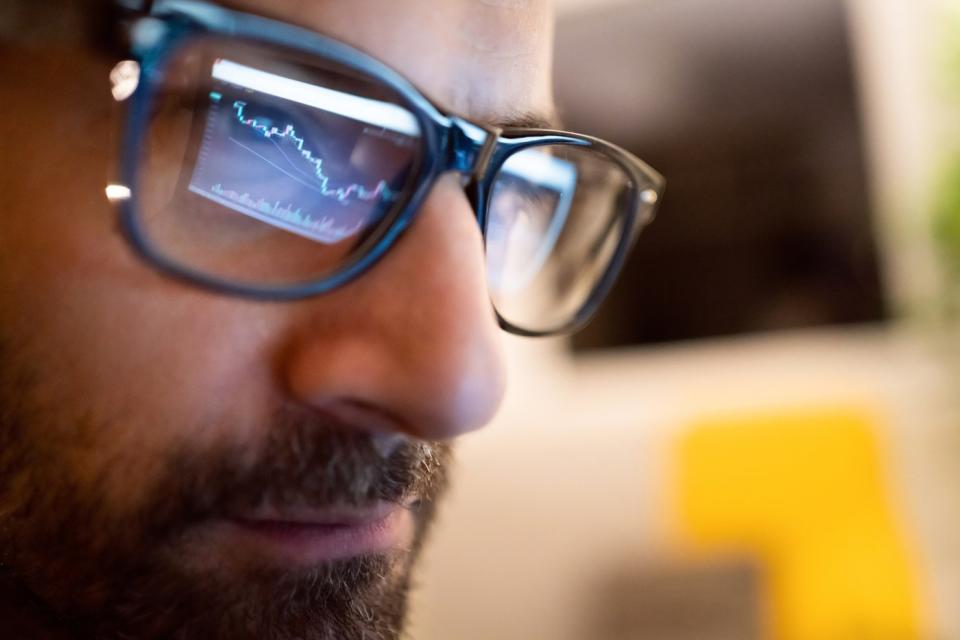 A stock chart displayed on a computer monitor being reflected in the eyeglasses of a professional money manager.