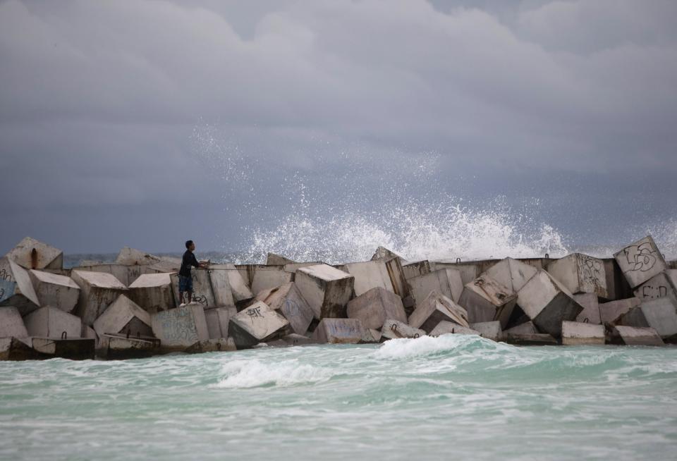 A man fishes while standing on wave breakers in Cancun