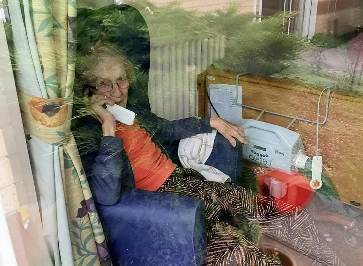 Elizabeth Bow talking to relatives on the phone through the closed window of her care home. (SWNS)