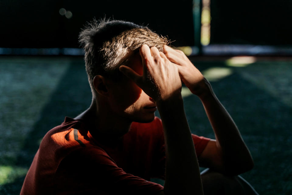 Person sitting outdoors, shielding eyes from sunlight, in a contemplative pose