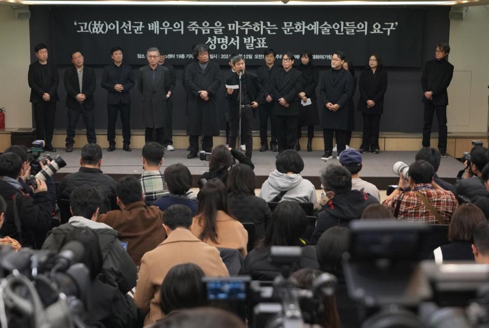 A line of people dressed in black standing onstage speaking to an audience